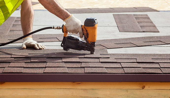 Asphalt roofing is being installed on a new roof by a worker.