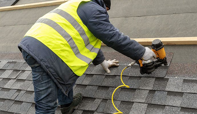Installing roof tiles with a pneumatic nail gun by a worker